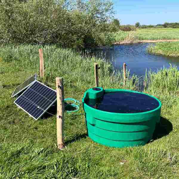 Solarbetriebene Feldpumpe mit Solarpanel und Wassertrog an einem Bach auf einer Wiese