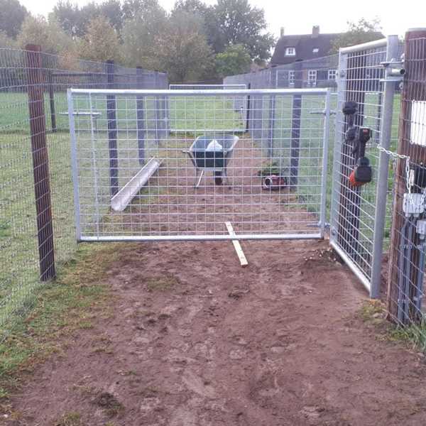 Eine Schubkarre steht hinter einem Leichttore mit Gitter.